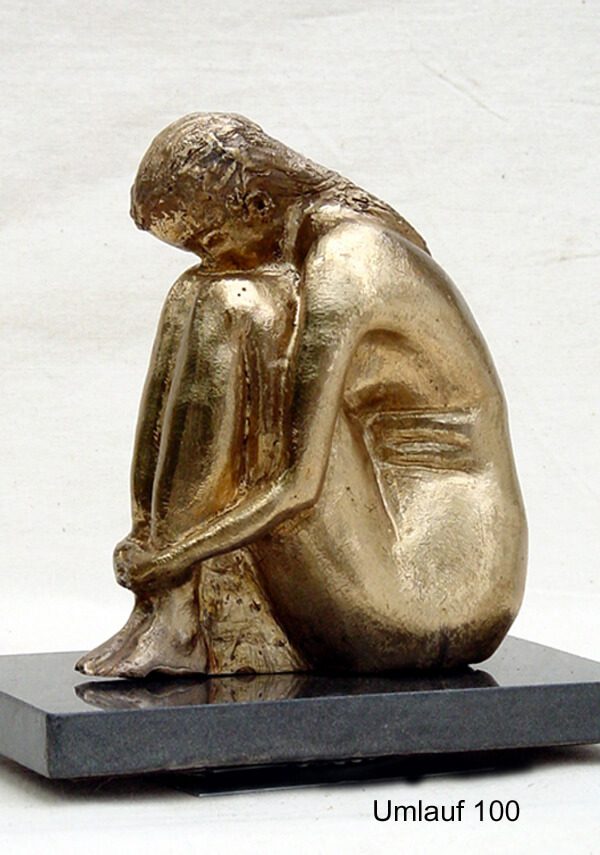 A gold statue of a person sitting on top of a black pedestal.