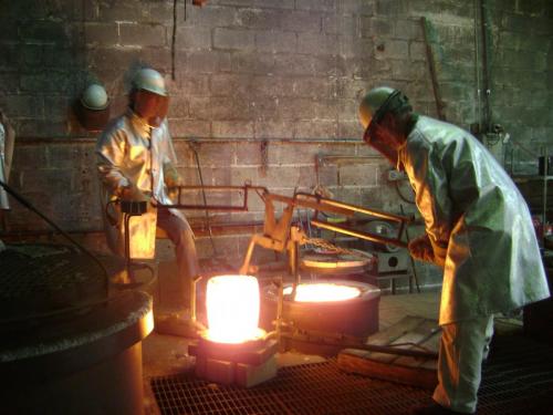 Two men working in a foundry with a large metal object.