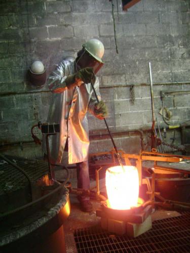 A man in white coat and hard hat working with metal.