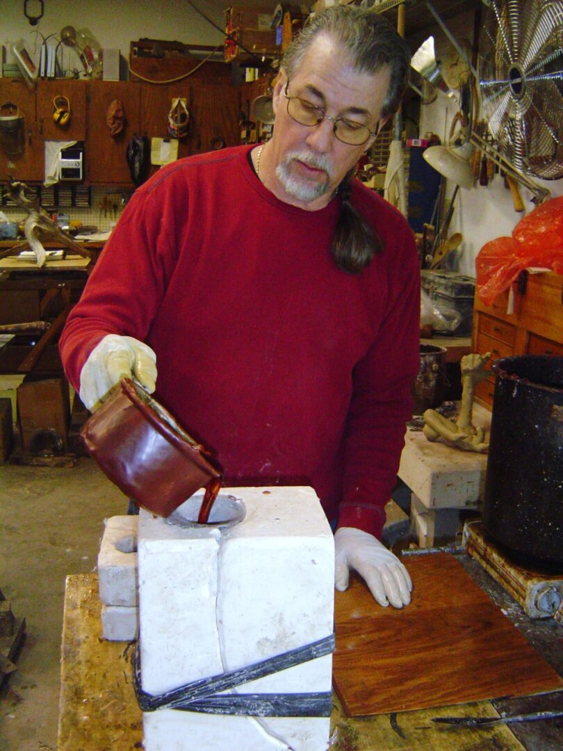 A man wearing a red sweater is making a mother mold for a sculpting project.
