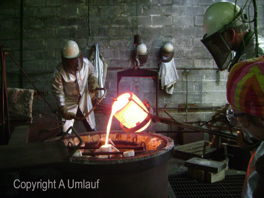 Two men working in a factory, using the ceramic shell mold process with molten metal.