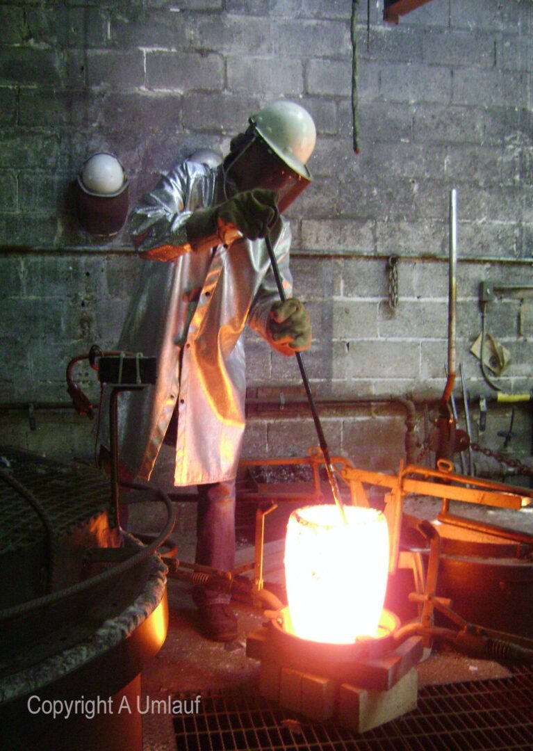 A men working in a factory, using the ceramic shell mold process with molten metal.