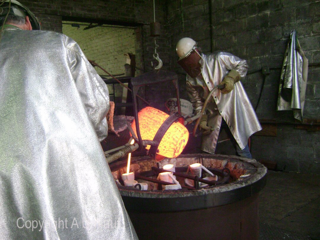 Two men working in a factory, using the ceramic shell mold process with molten metal.