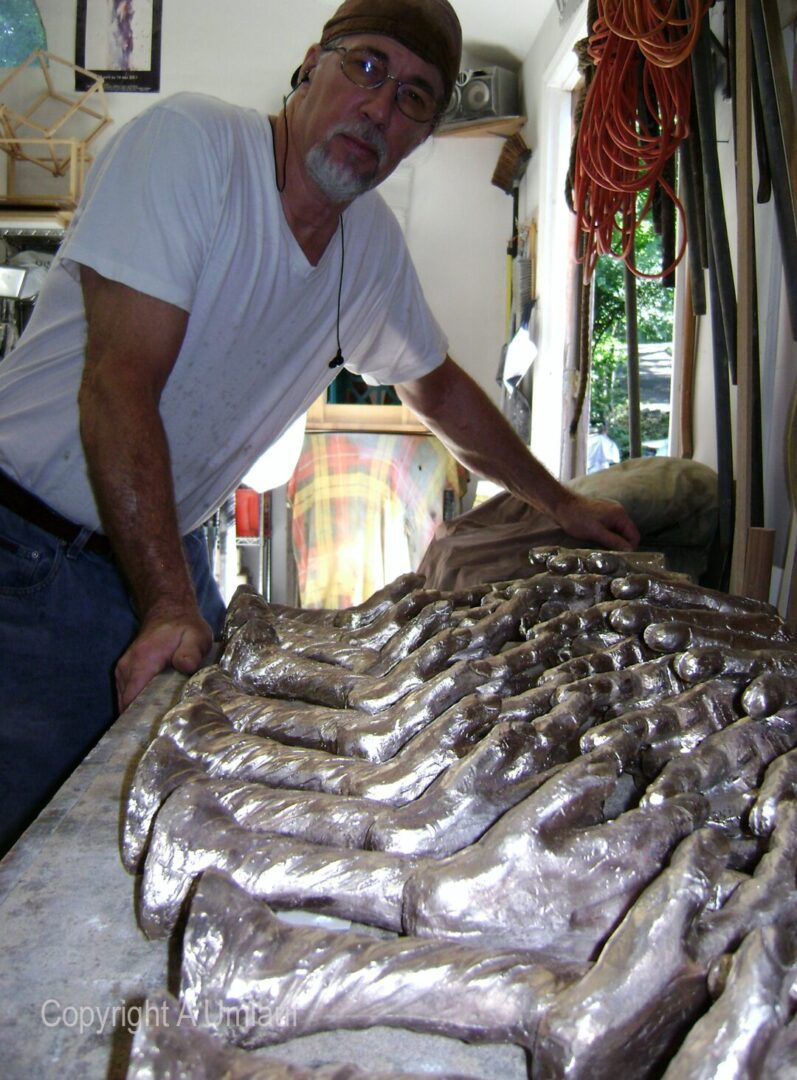 A man standing in front of a pile of silver sculptures created using the Ceramic Shell Mold Process.