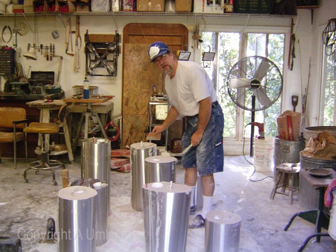 A man utilizing the investment mold method to pour cement into two metal buckets.