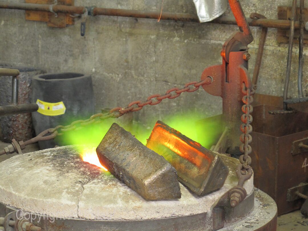In the UmlaufGallery, a furnace is emitting a vibrant green flame as bronze is being poured.