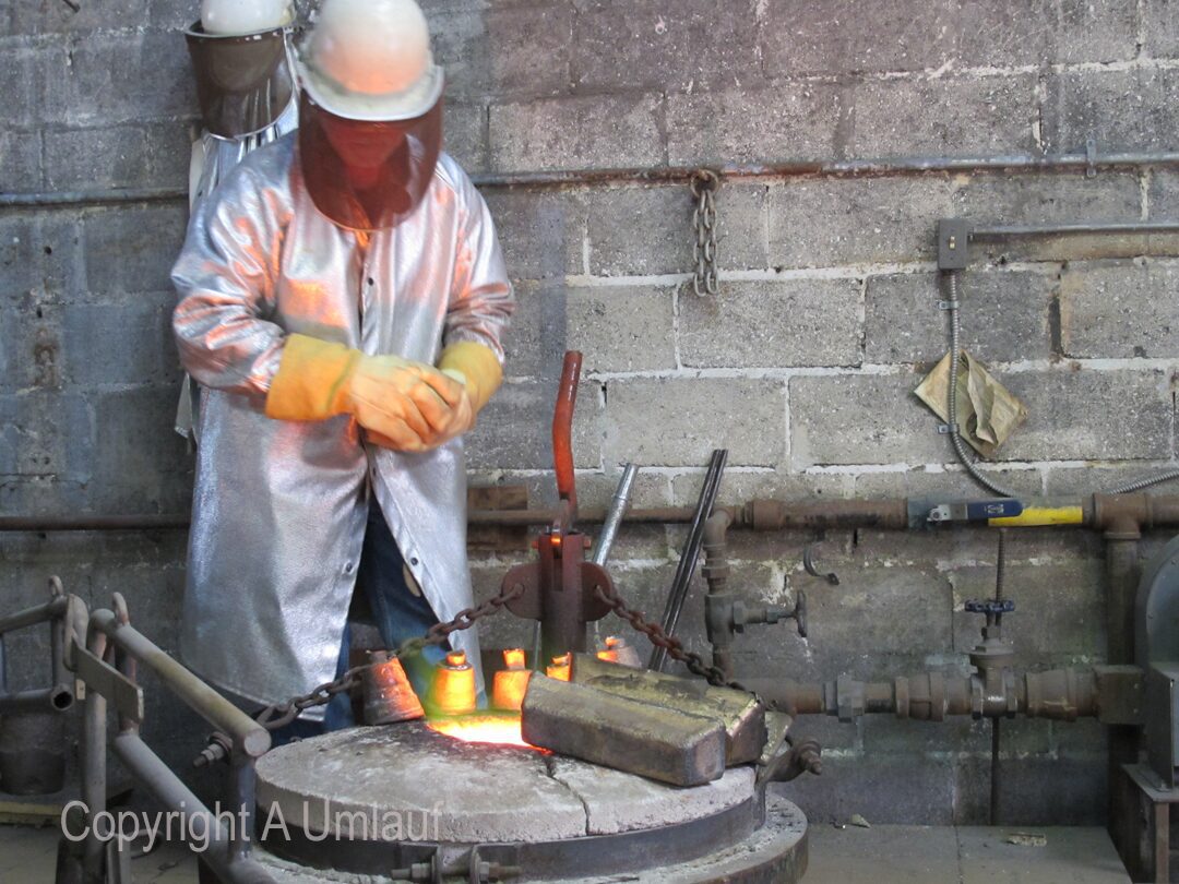 A man in a hard hat is working on pouring bronze onto a piece of metal at the Umlauf Gallery.