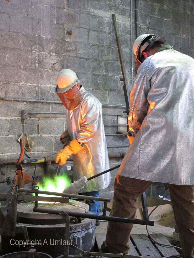 Two men working in a UmlaufGallery furnace, pouring bronze.