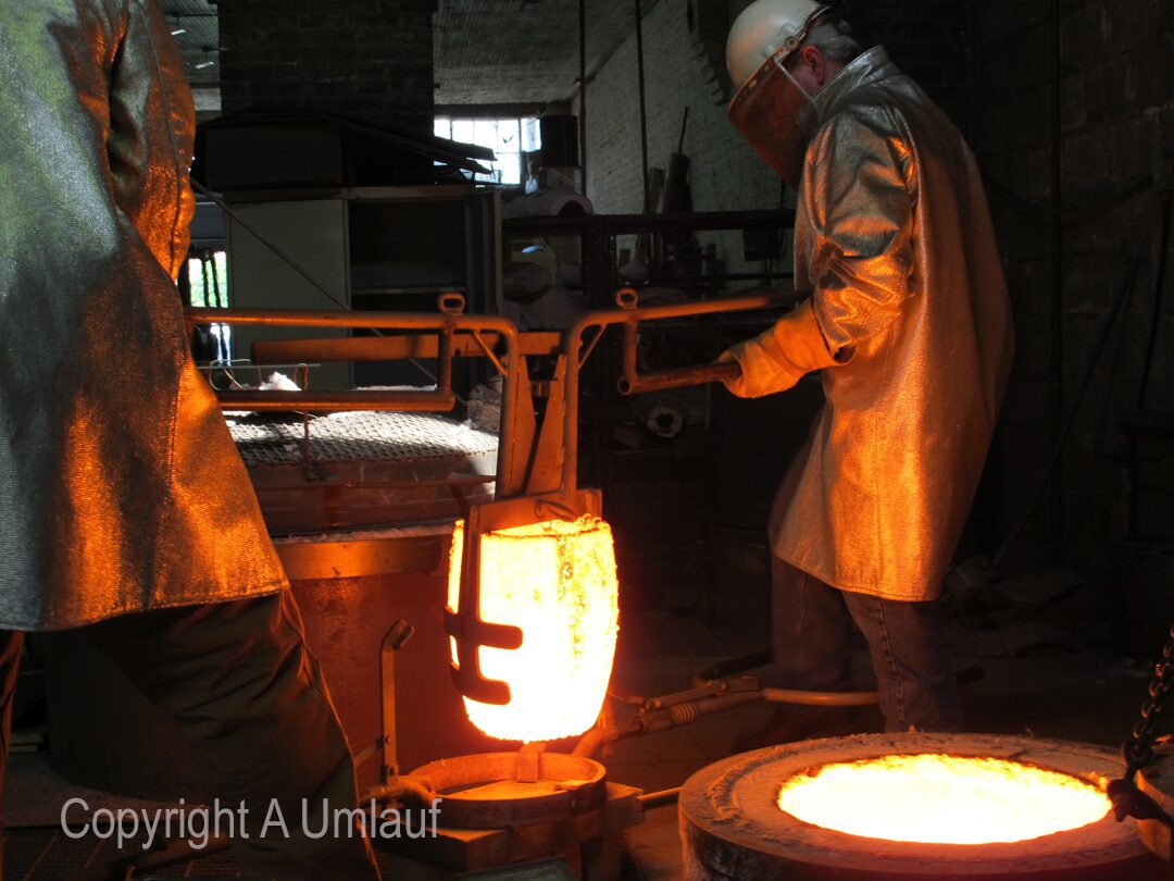 Two men working in a UmlaufGallery furnace, pouring bronze.