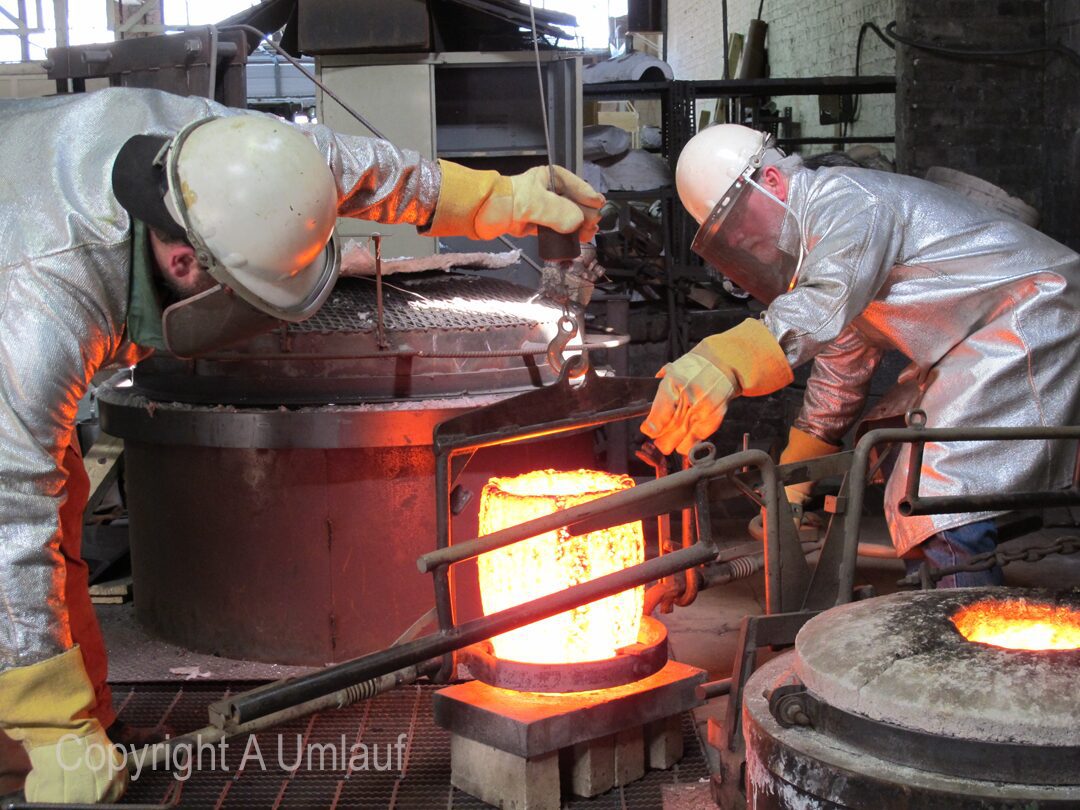 Two men working in a factory pouring molten metal.