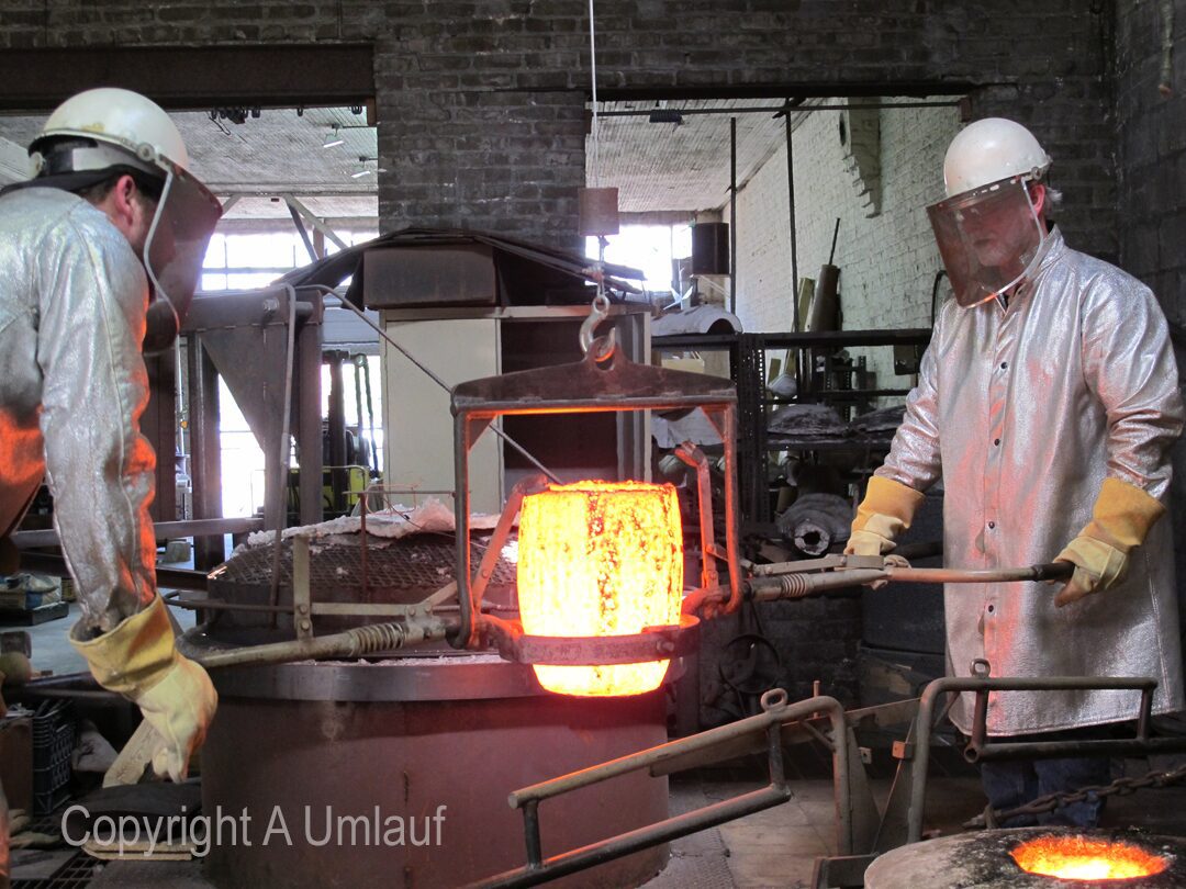 Two men working in a factory pouring molten metal.