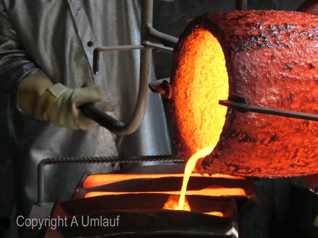 A man is pouring molten metal into a furnace at the UmlaufGallery.