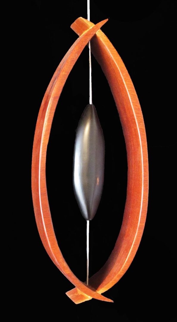 An orange and black pendant hanging from a black background on display at an art gallery exhibition.