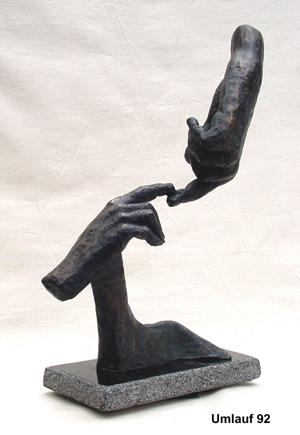 A bronze sculpture of a hand reaching out to another displayed in a Fine Art Gallery.