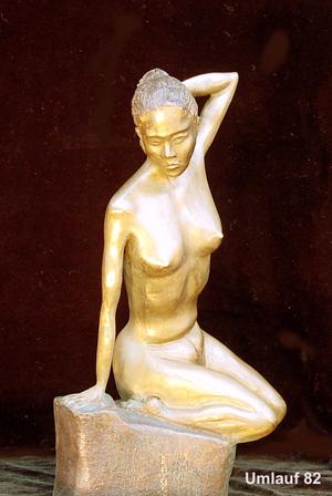 A bronze statue of a woman sitting on a rock displayed in a Fine Art Gallery.