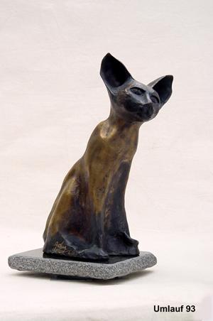 A bronze sculpture of a cat sitting on a stone displayed in a Fine Art Gallery.